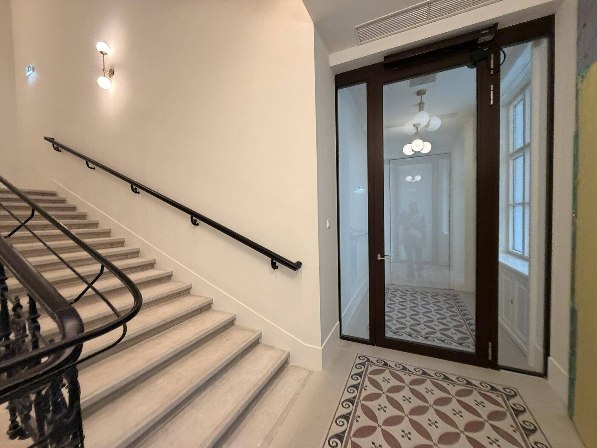 Helles Treppenhaus mit Handlauf und einer modernen Glastür, die den Zugang zum Flur ermöglicht.
