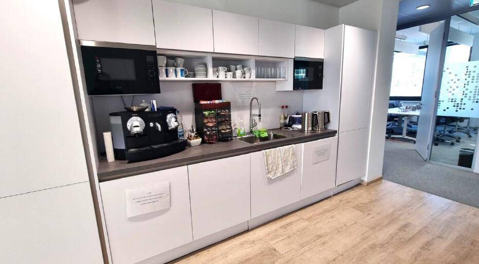 Moderne Küchenzeile mit weißen Schränken, integrierten Geräten und einer Kaffeemaschine für die Mitarbeiter.