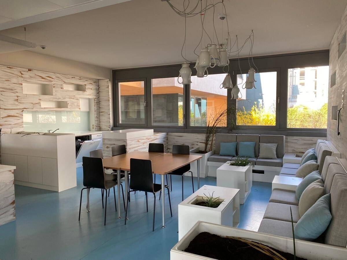 Heller Lounge-Bereich mit blauer Bodenfarbe, bequemen Sofas und einer kleinen Küchenzeile.
