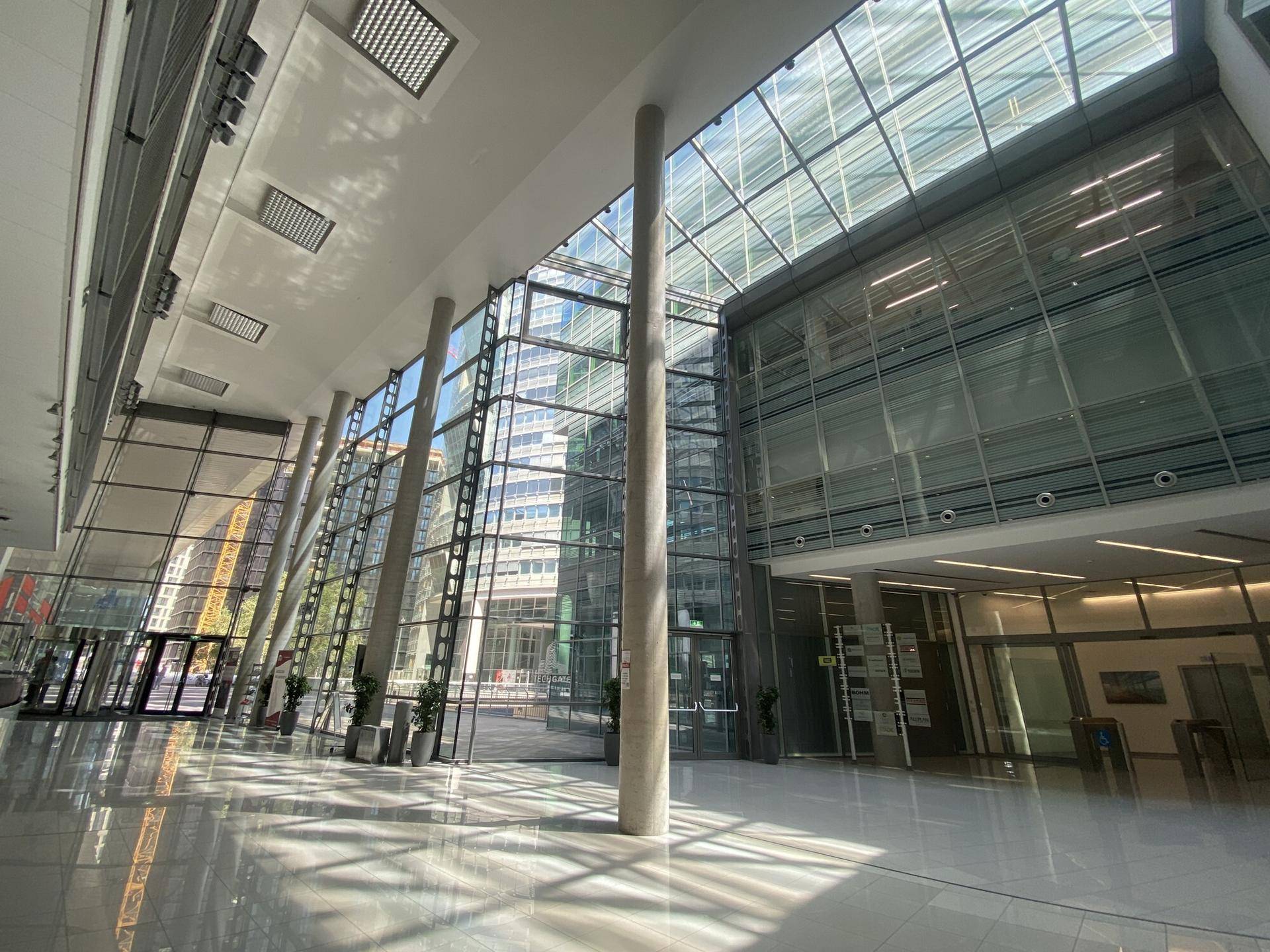 Weitläufige, lichtdurchflutete Lobby mit hohen Glaswänden und Säulen, die eine moderne Atmosphäre schafft.