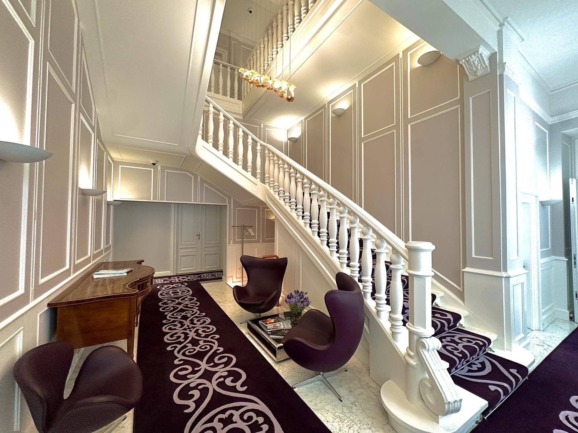 Prächtiges Foyer mit einer eleganten Treppe, gemustertem Teppich und stilvollen Sesseln.