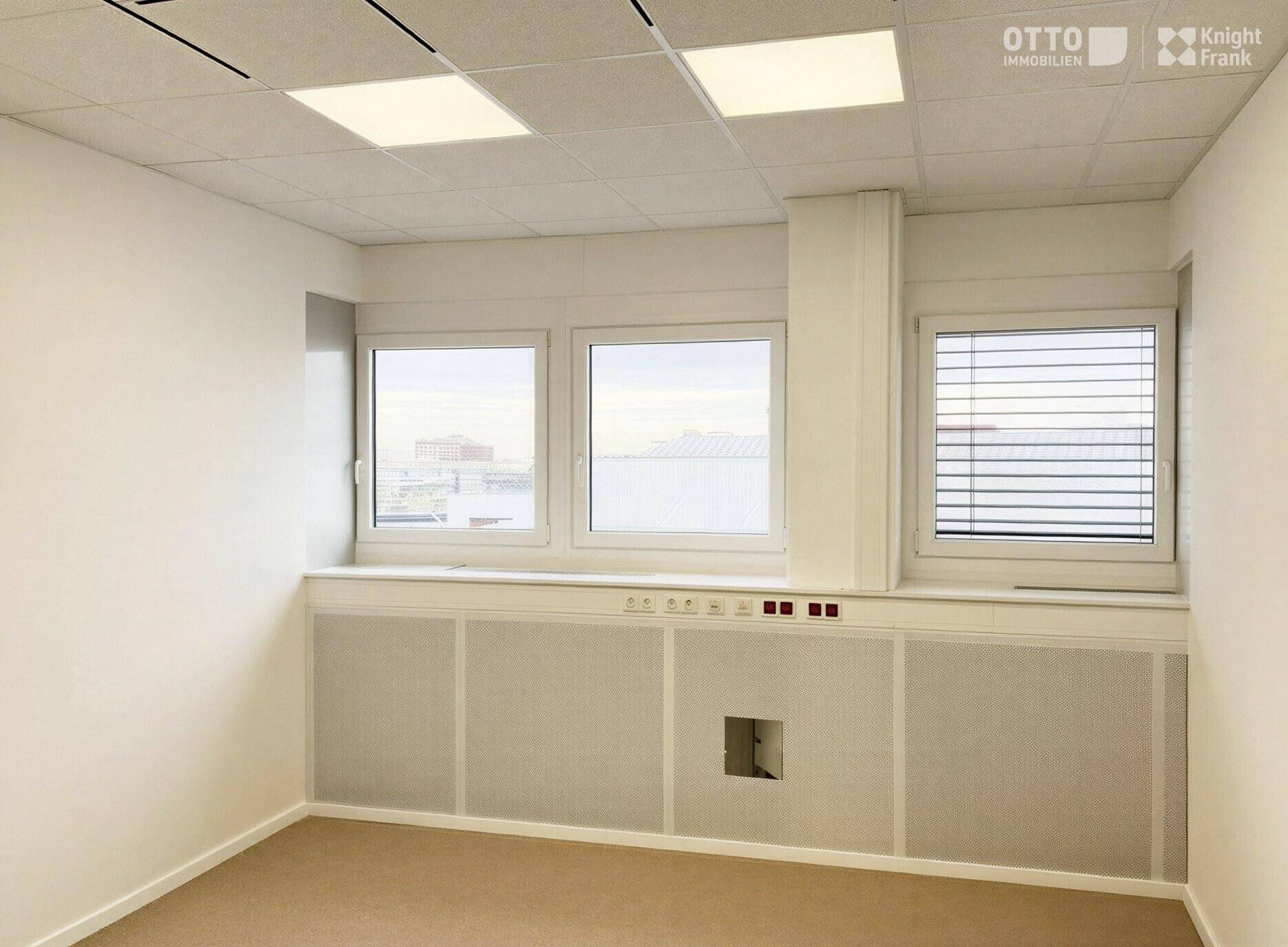Heller Büroraum mit Fenster und Jalousien, ausgestattet mit praktischen Wandanschlüssen.