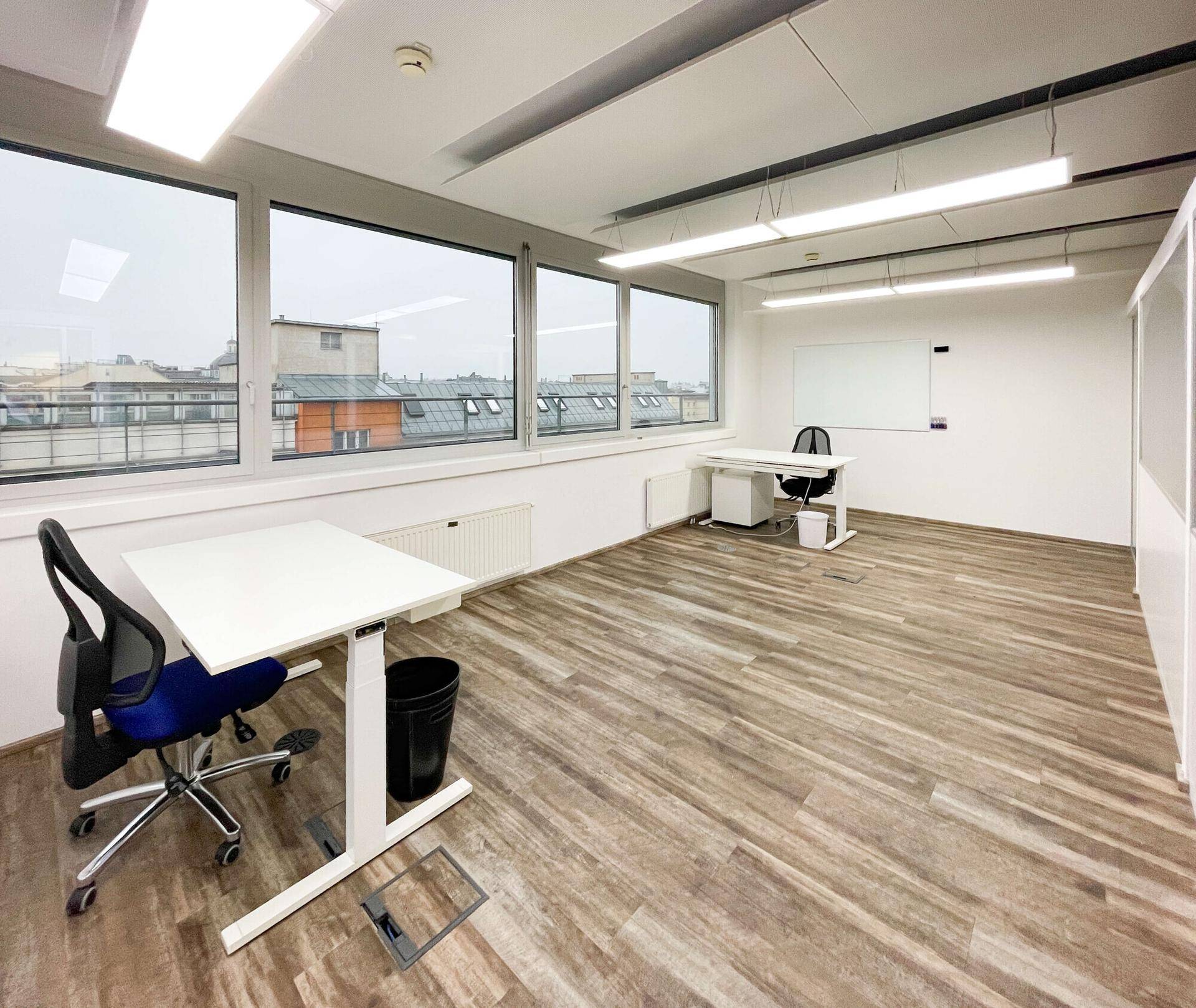 Leeres, helles Büro mit einem einzelnen Schreibtisch, großen Fenstern und Holzboden.
