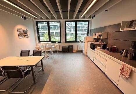 Helle Büroküche mit weißen Schränken, dunkler Arbeitsplatte und Essbereich, ausgestattet für Mitarbeiter.