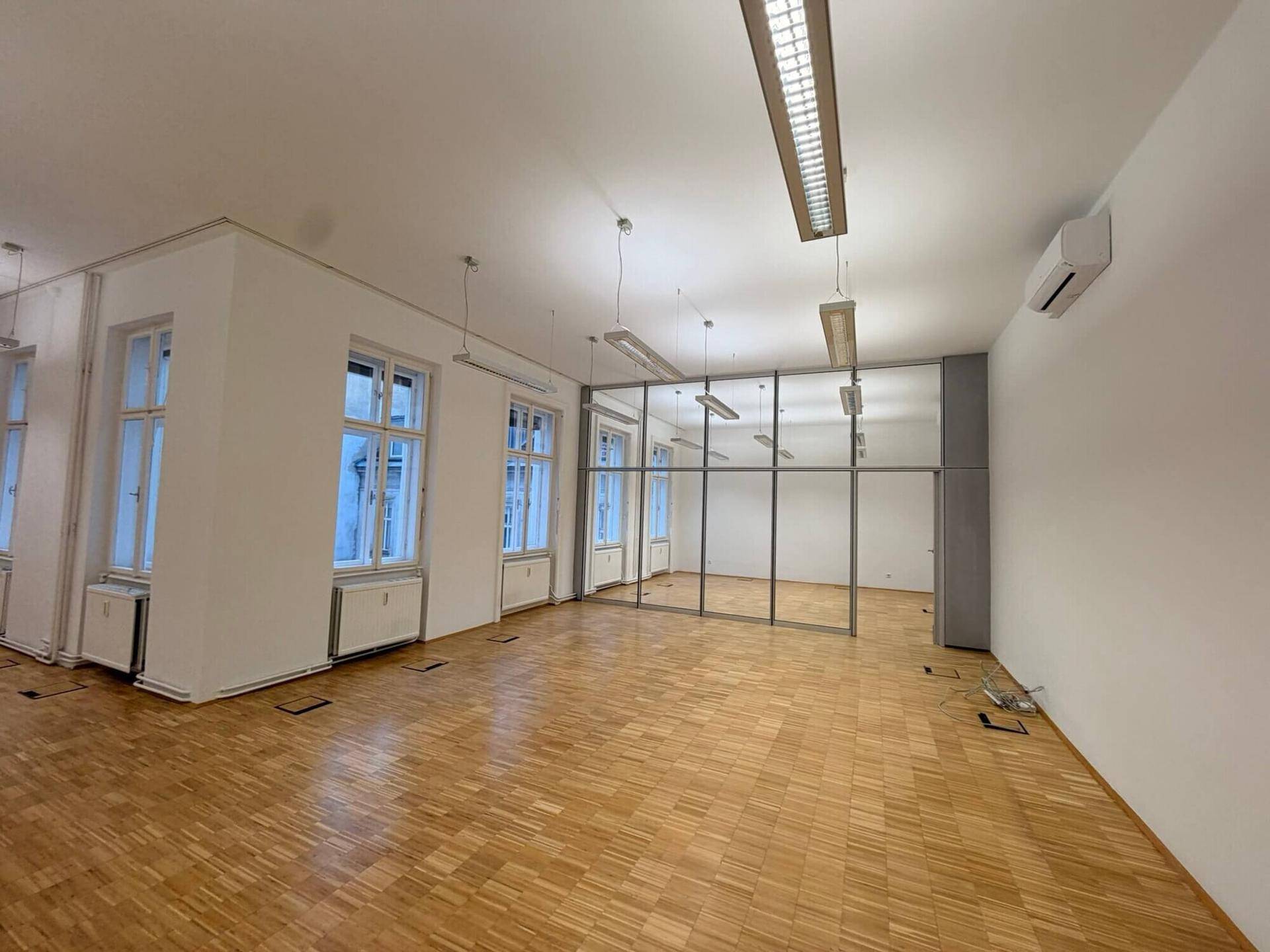 Geräumiger Bürobereich mit Parkettboden, großen Fenstern, Glasabtrennung und Klimaanlage, ideal für flexible Arbeitsplatzlösungen.