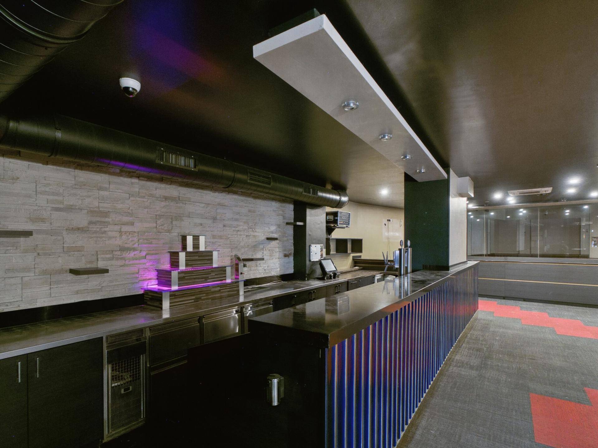 Moderne Bar mit langer Theke, Steinwand und integrierten Beleuchtungseffekten.