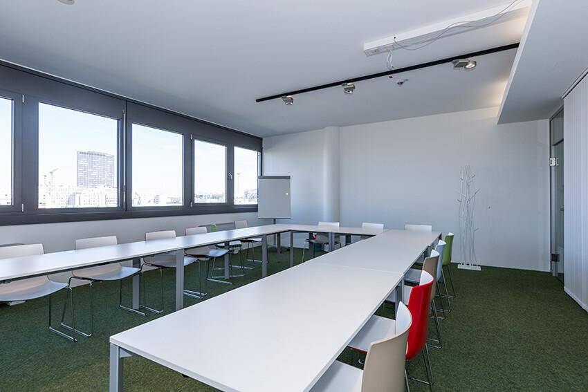 Großer Konferenzraum mit U-förmiger Tischordnung, grüner Teppichboden und weitem Ausblick.