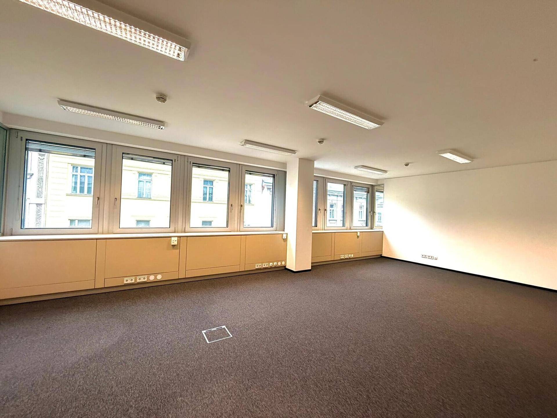 Geräumiger Bürobereich mit umlaufender Fensterfront, Teppichboden und moderner Deckenbeleuchtung.
