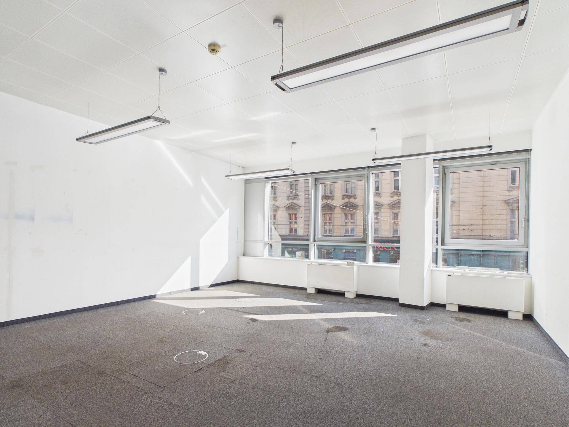 Geräumiges Büro mit großen Fenstern, die viel Tageslicht hereinlassen und Blick auf die Stadt bieten.