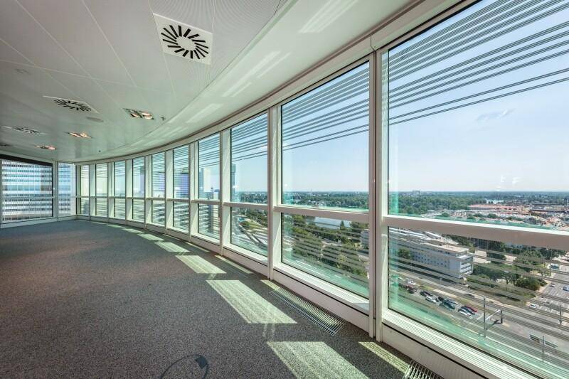 Geräumiger, leerer Büroraum mit gebogener Glasfassade und weitem Blick über die Stadt und die Umgebung.