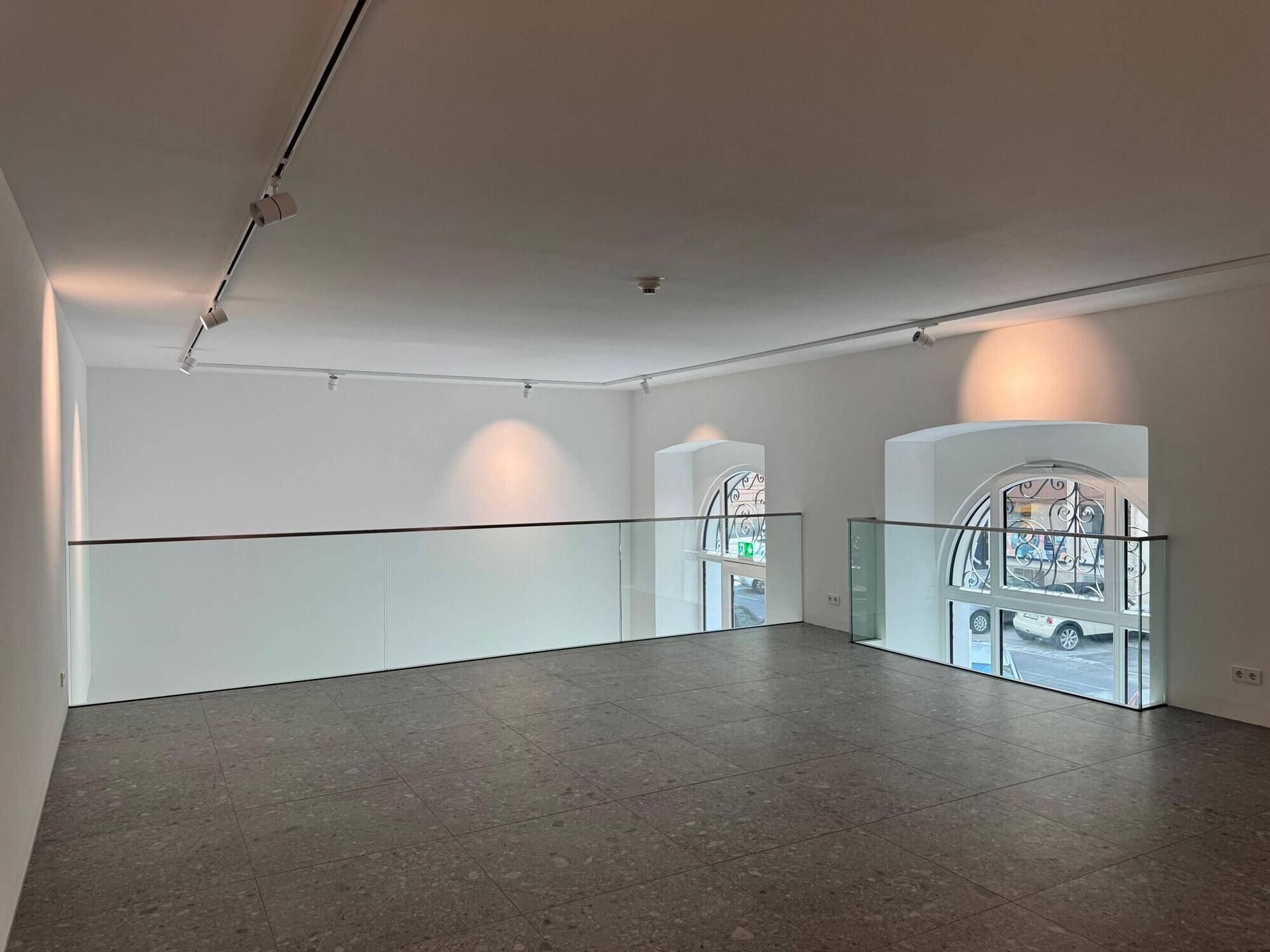 Geräumige Galeriefläche mit minimalistischem Design, Glasgeländer und Blick auf die Fensterfronten des Erdgeschosses.