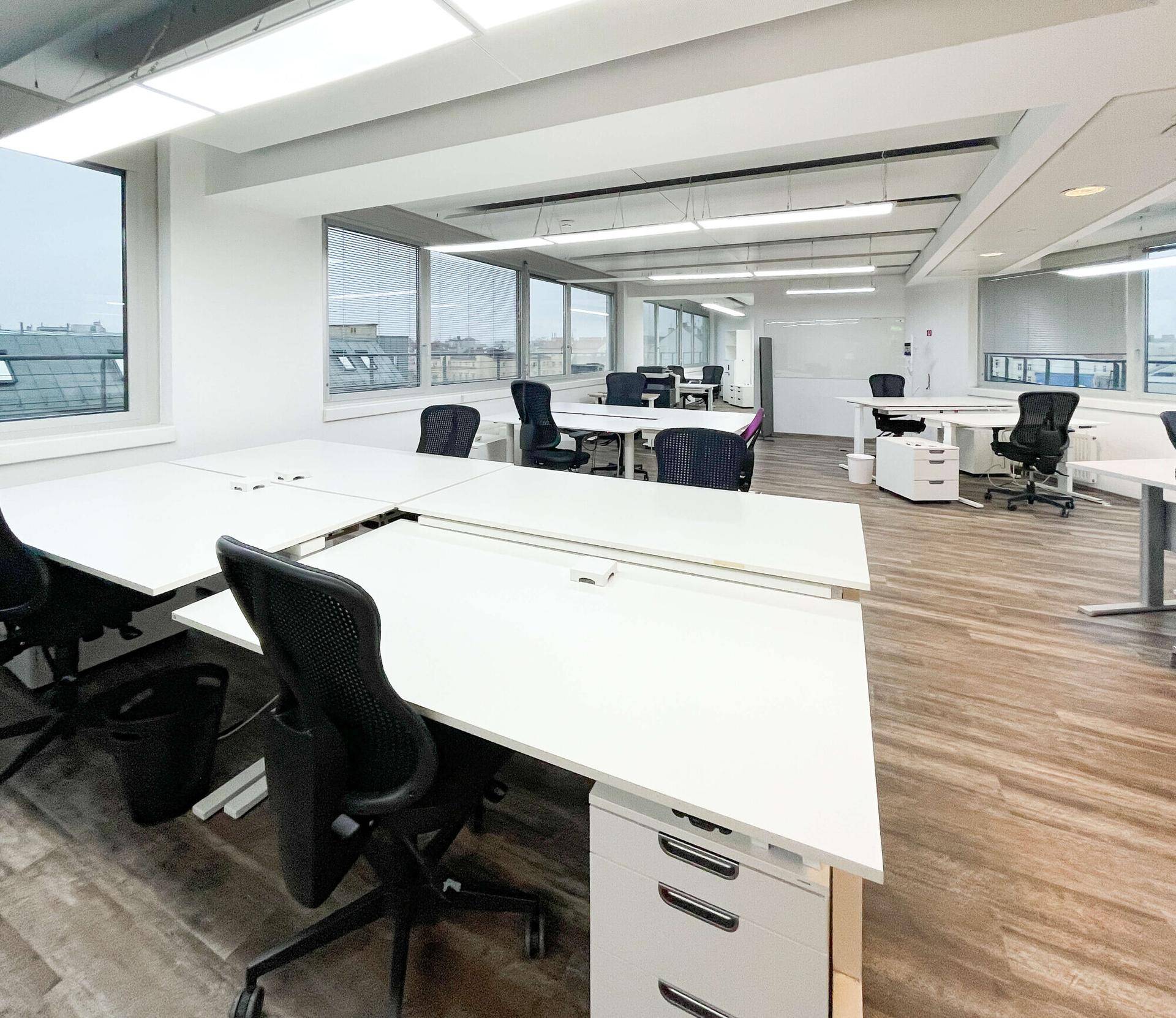 Geräumiges und helles Büro mit mehreren Schreibtischen, ergonomischen Stühlen und Laminatboden.