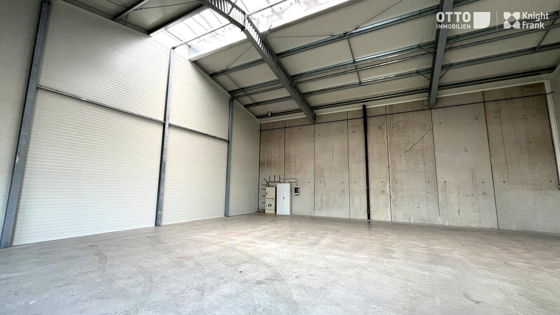 Helle Lagerhalle mit hohen Decken, sichtbaren Trägern und Oberlichtern für natürliche Beleuchtung.