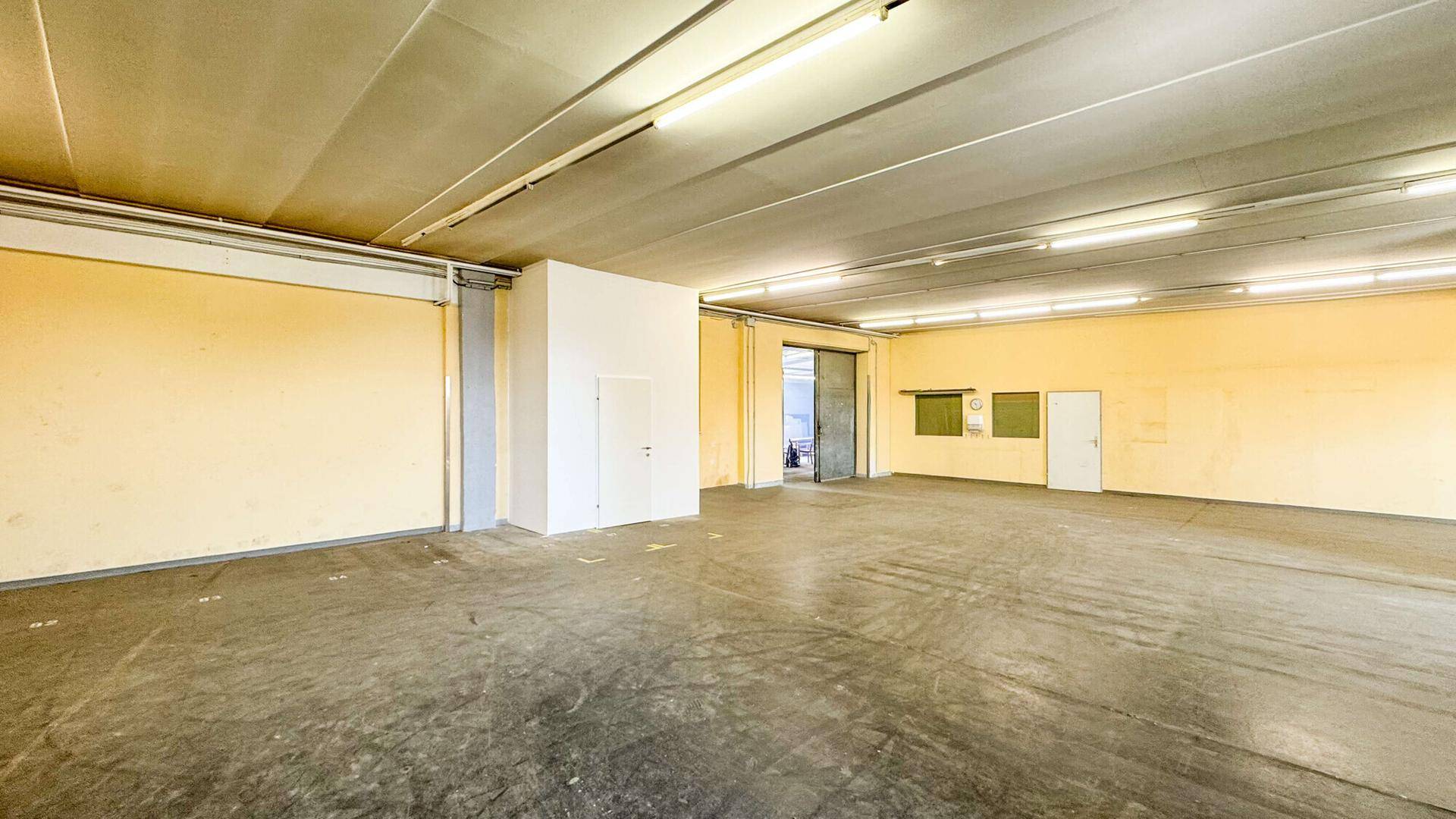 Weitläufiger Lagerraum mit gelben Wänden, Betonboden und einem großen Schiebetor, das den Zugang ermöglicht.