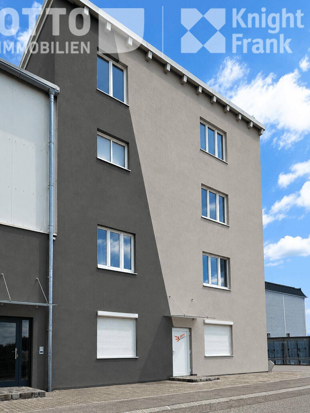 Mehrstöckiges Gebäude mit zweifarbiger Fassade, vielen Fenstern und Rollläden unter blauem Himmel.