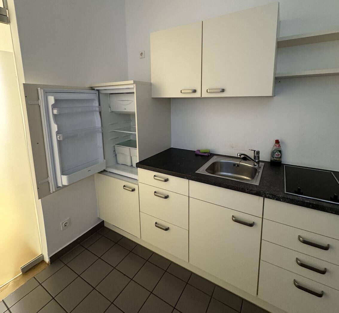 Kleine Küchenzeile mit Kühlschrank, Spüle und Kochfeld, ideal für eine Büroküche oder Teeküche.