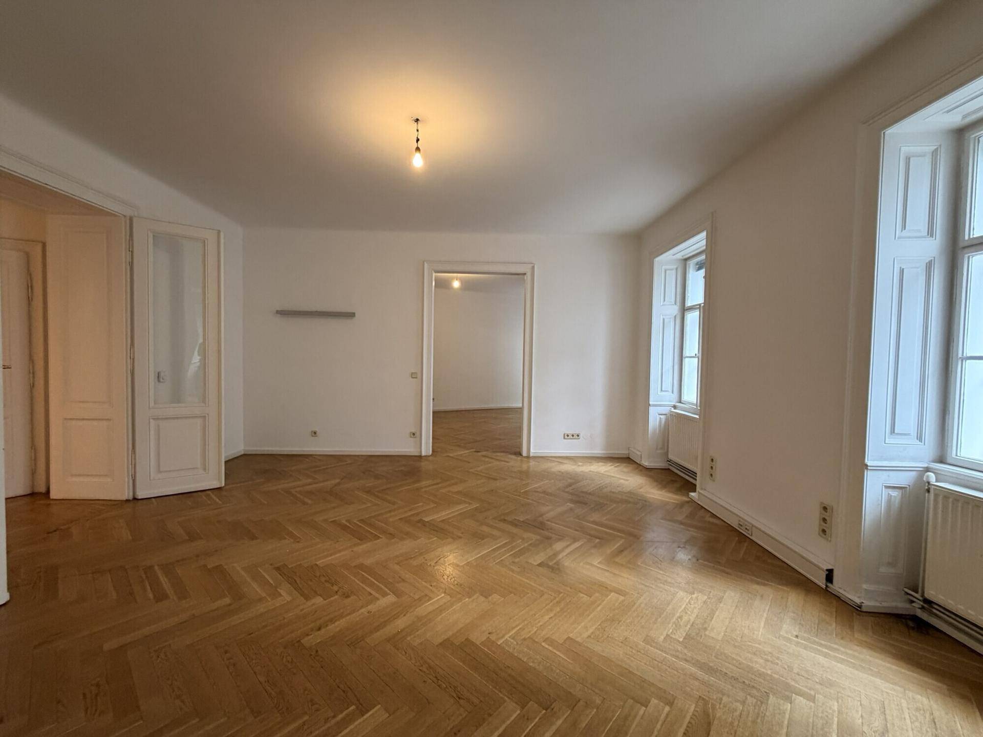 Helles Wohnzimmer mit klassischem Fischgrätparkett und hohen Doppeltüren, die zu weiteren Räumen führen.