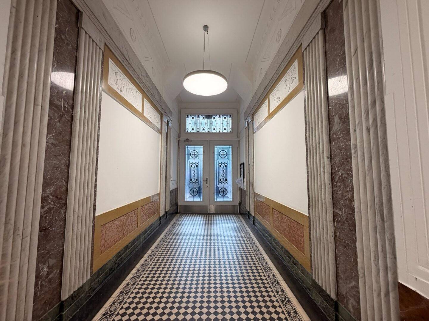 Eleganter Flur mit Schachbrettmuster-Fliesenboden, Marmorverkleidung und verzierten Eingangstüren.