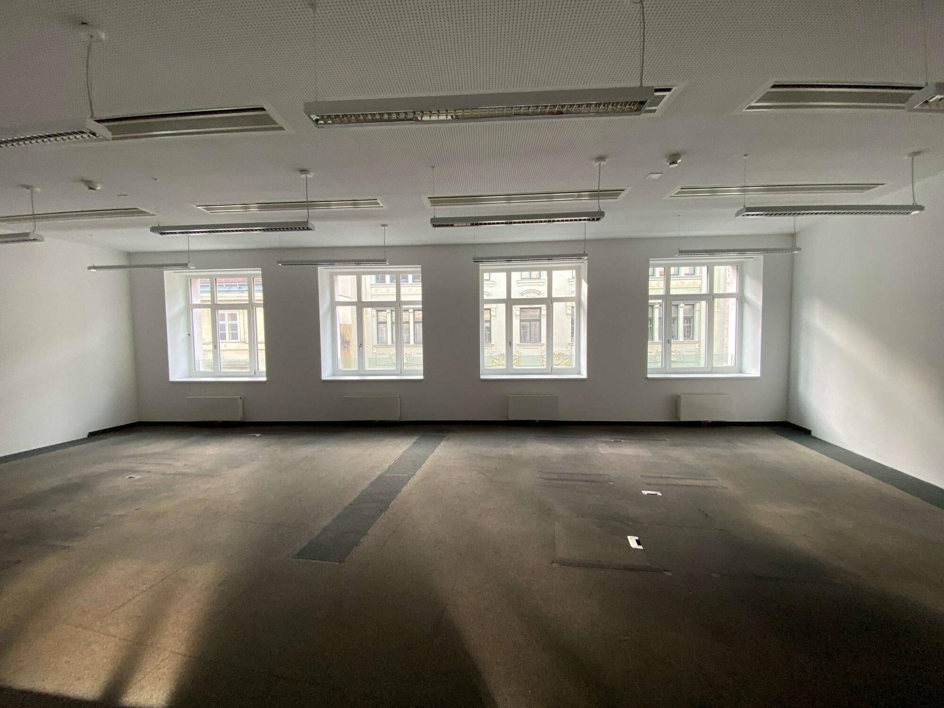 Leerer Büroraum mit Teppichboden, großen Fenstern und funktionaler Deckenbeleuchtung, bereit zur individuellen Gestaltung.
