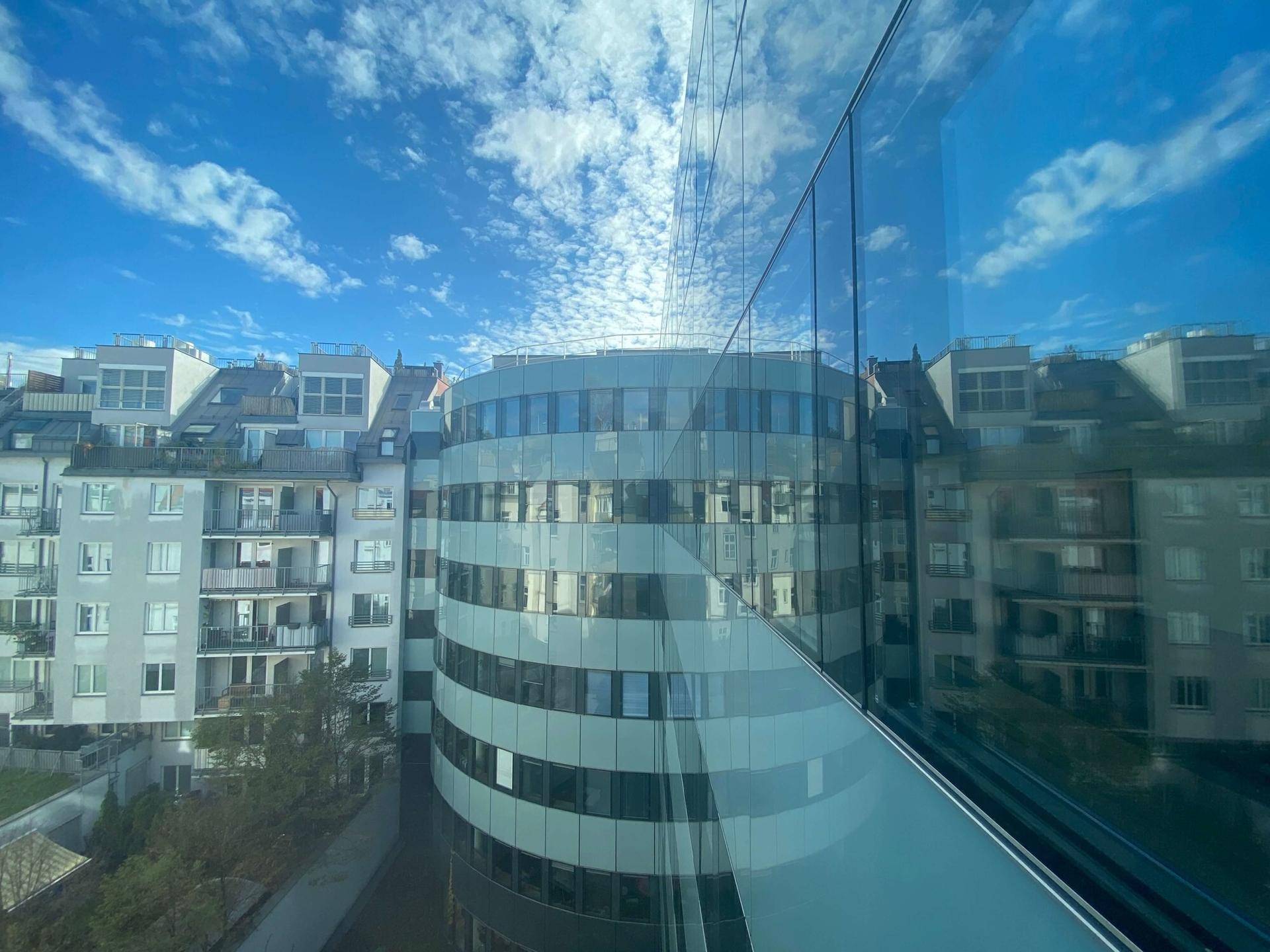 Blick aus einem Fenster auf die umliegenden Gebäude und den blauen Himmel mit Wolken.