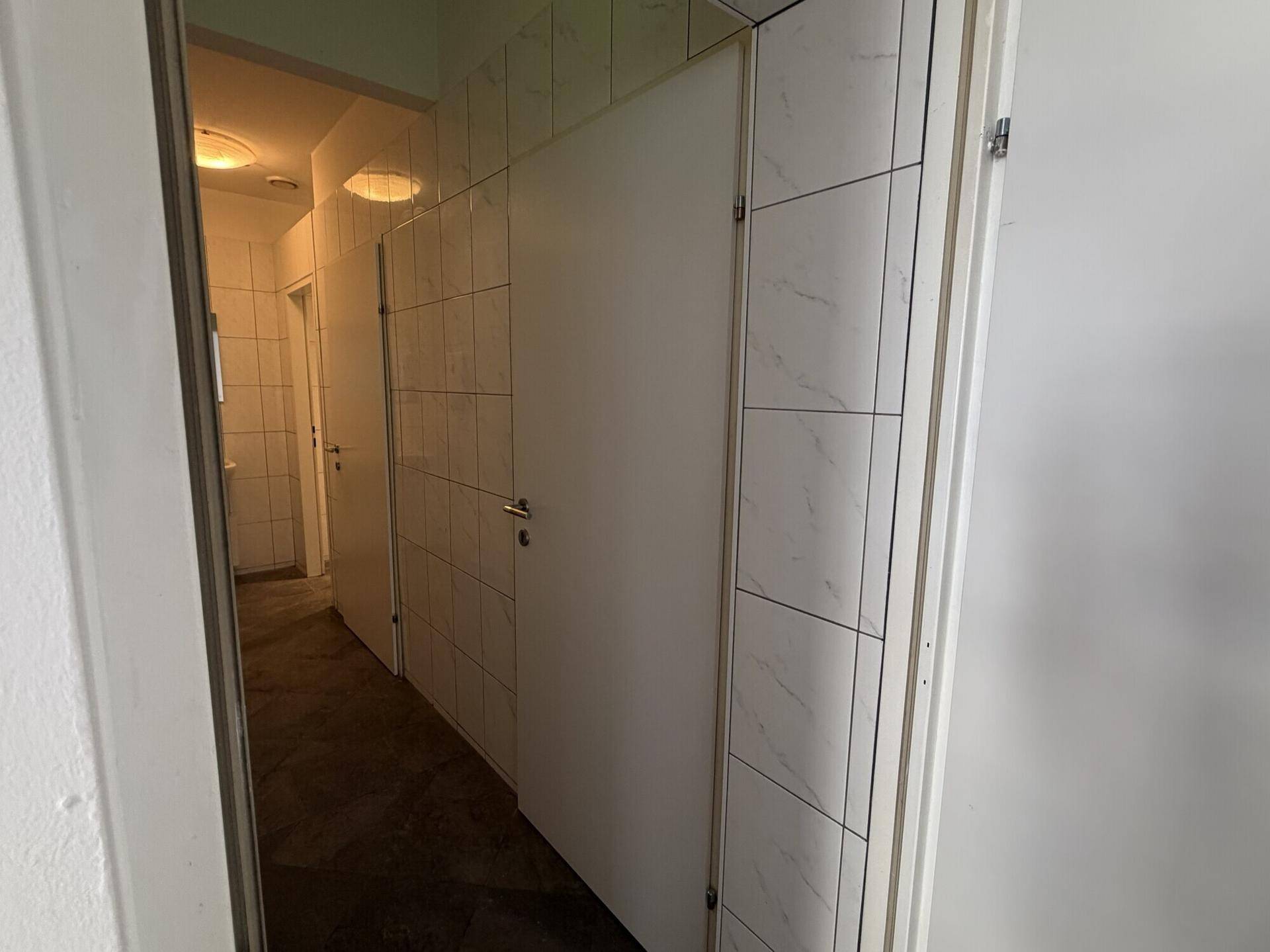 Gefliester Flur mit mehreren Türen, der zu den Toilettenräumen führt.