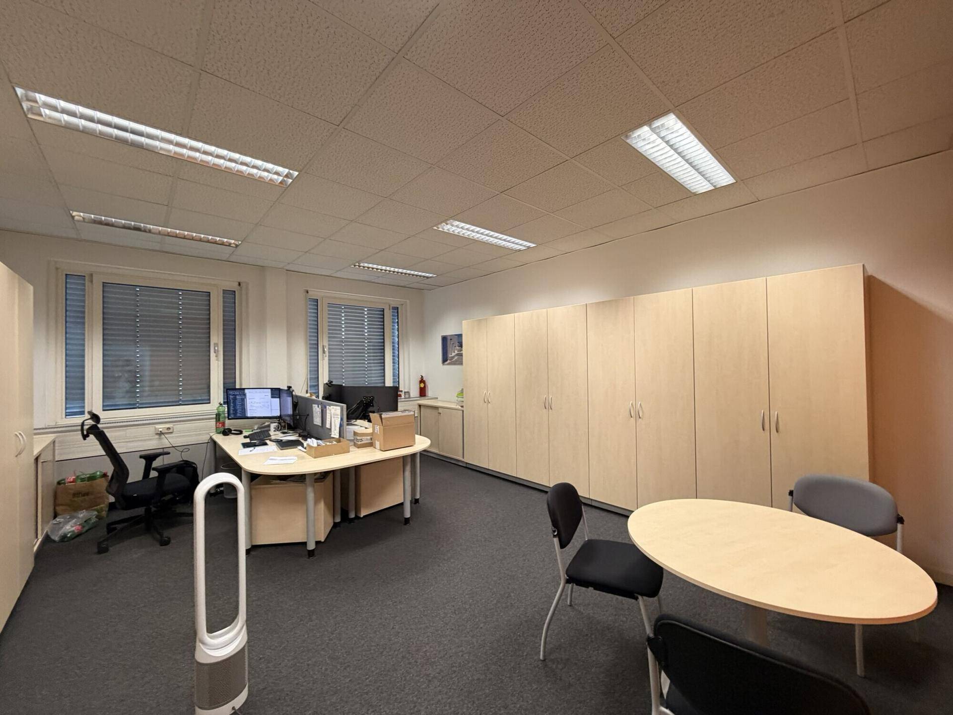 Helles Büro mit mehreren Arbeitsplätzen, Einbauschränken und Teppichboden.