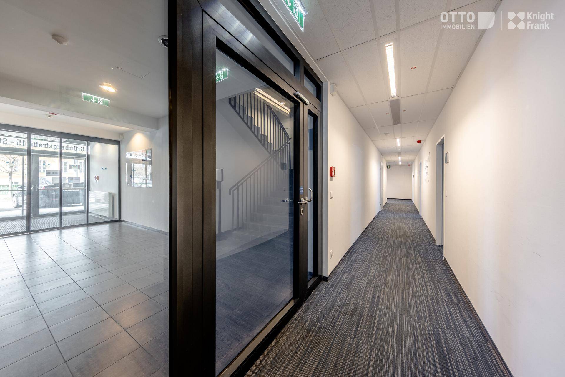 Langer, heller Flur mit Teppichboden und abgehängter Decke, der zu einem Eingangsbereich mit Treppe führt.