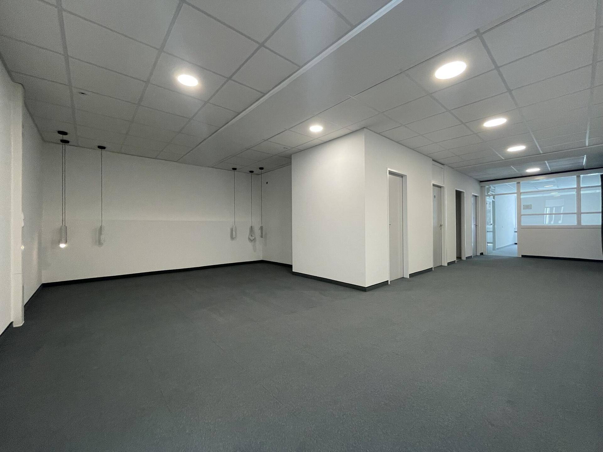 Geräumiger, leerer Bürobereich mit Teppichboden und moderner Deckenbeleuchtung.