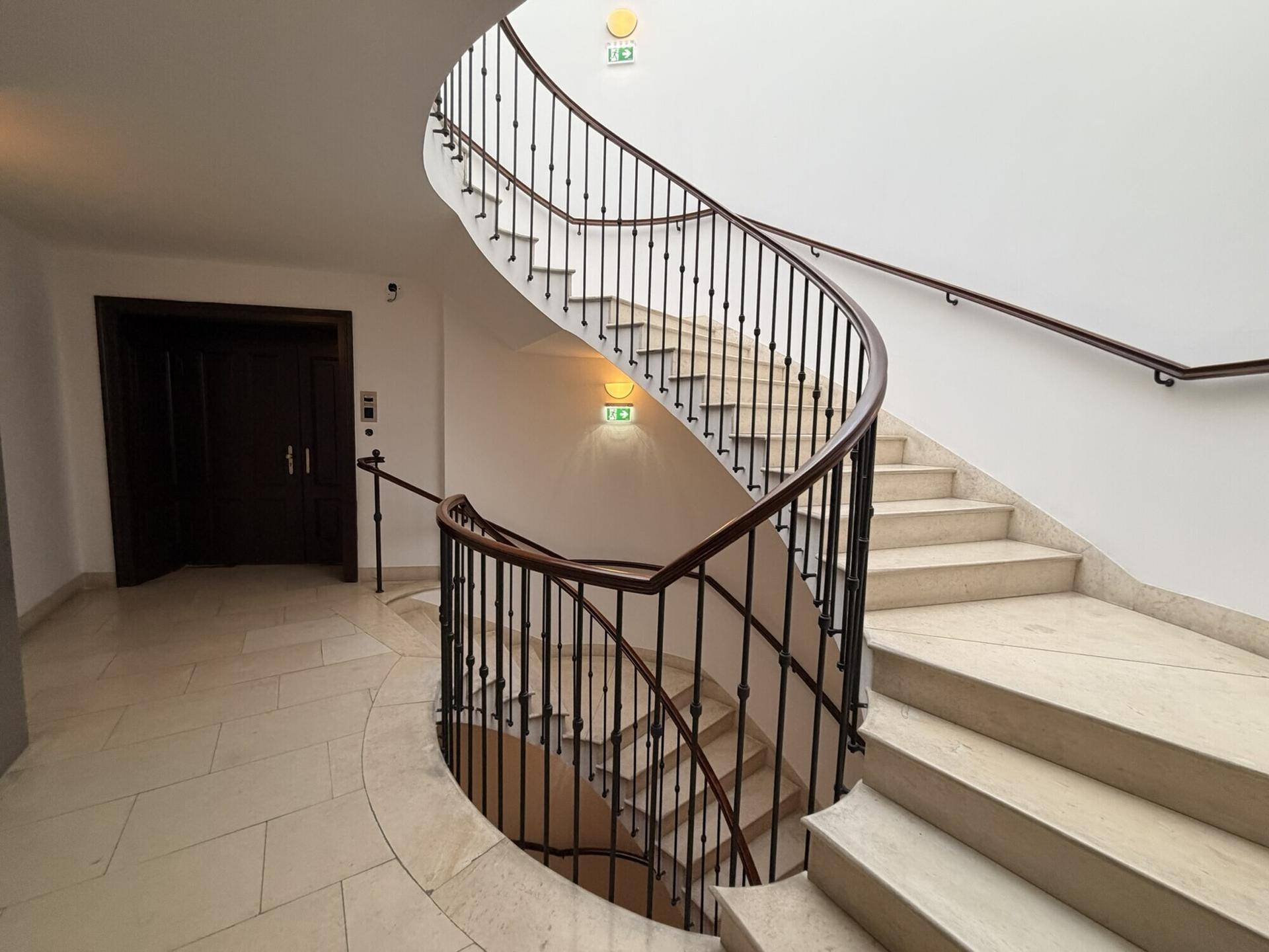 Elegante Wendeltreppe mit Marmorstufen und einem kunstvollen schmiedeeisernen Geländer in einem hellen Treppenhaus.