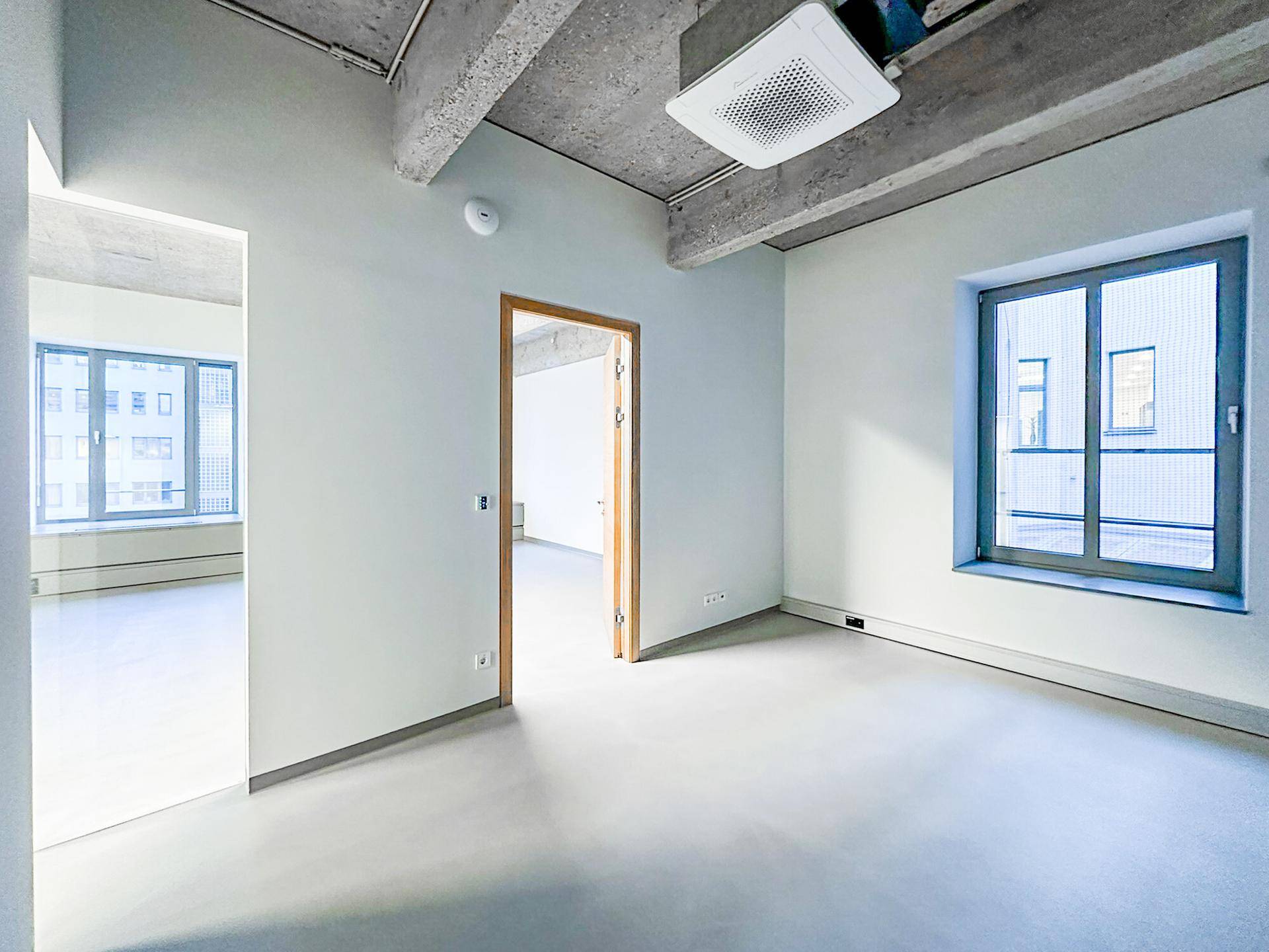 Heller Büroraum mit großen Fenstern und einer modernen Klimaanlage, ideal für flexible Arbeitsbereiche.