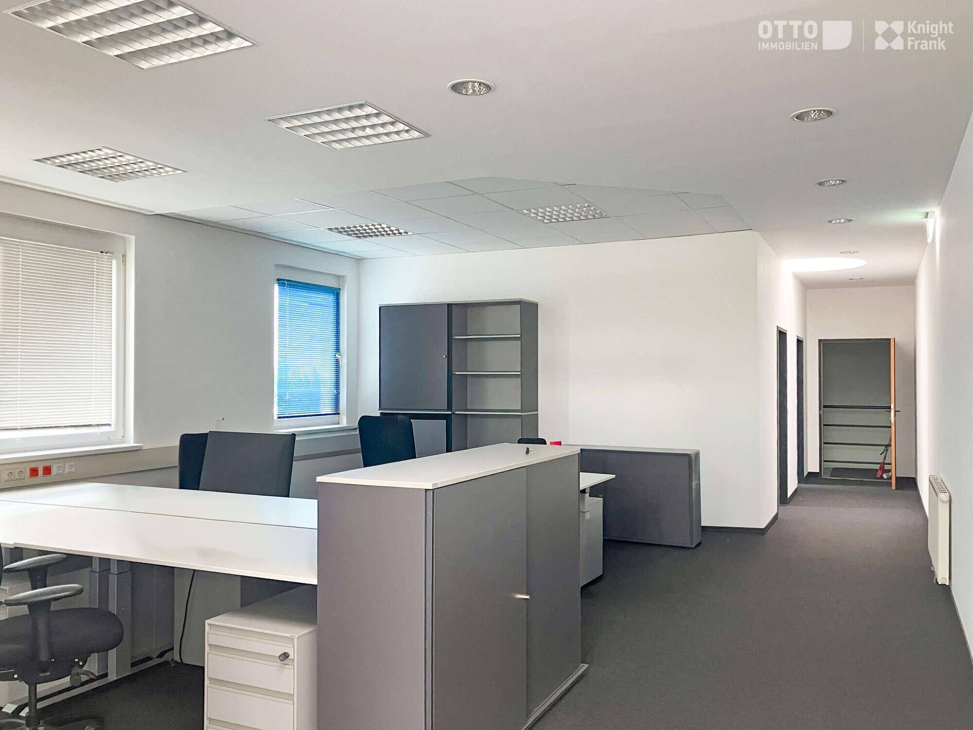 Helles und geräumiges Büro mit mehreren Arbeitsplätzen, Teppichboden und modernen Büromöbeln.