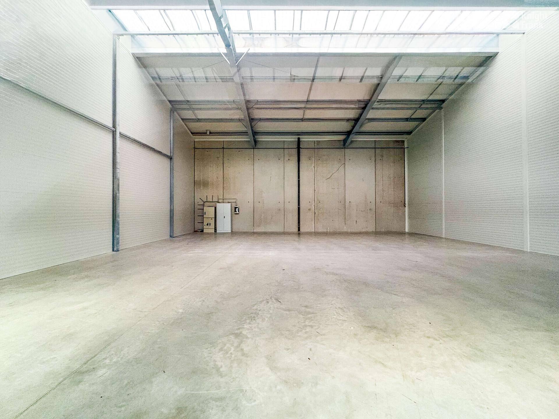 Geräumige, leere Lagerhalle mit hohen Decken, Betonwänden und Oberlichtern für natürliches Licht.