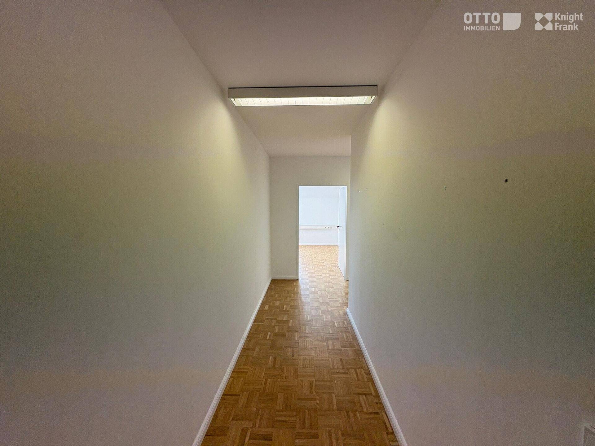 Schmaler Flur mit Parkettboden und weiß gestrichenen Wänden, der zu weiteren Räumen führt.