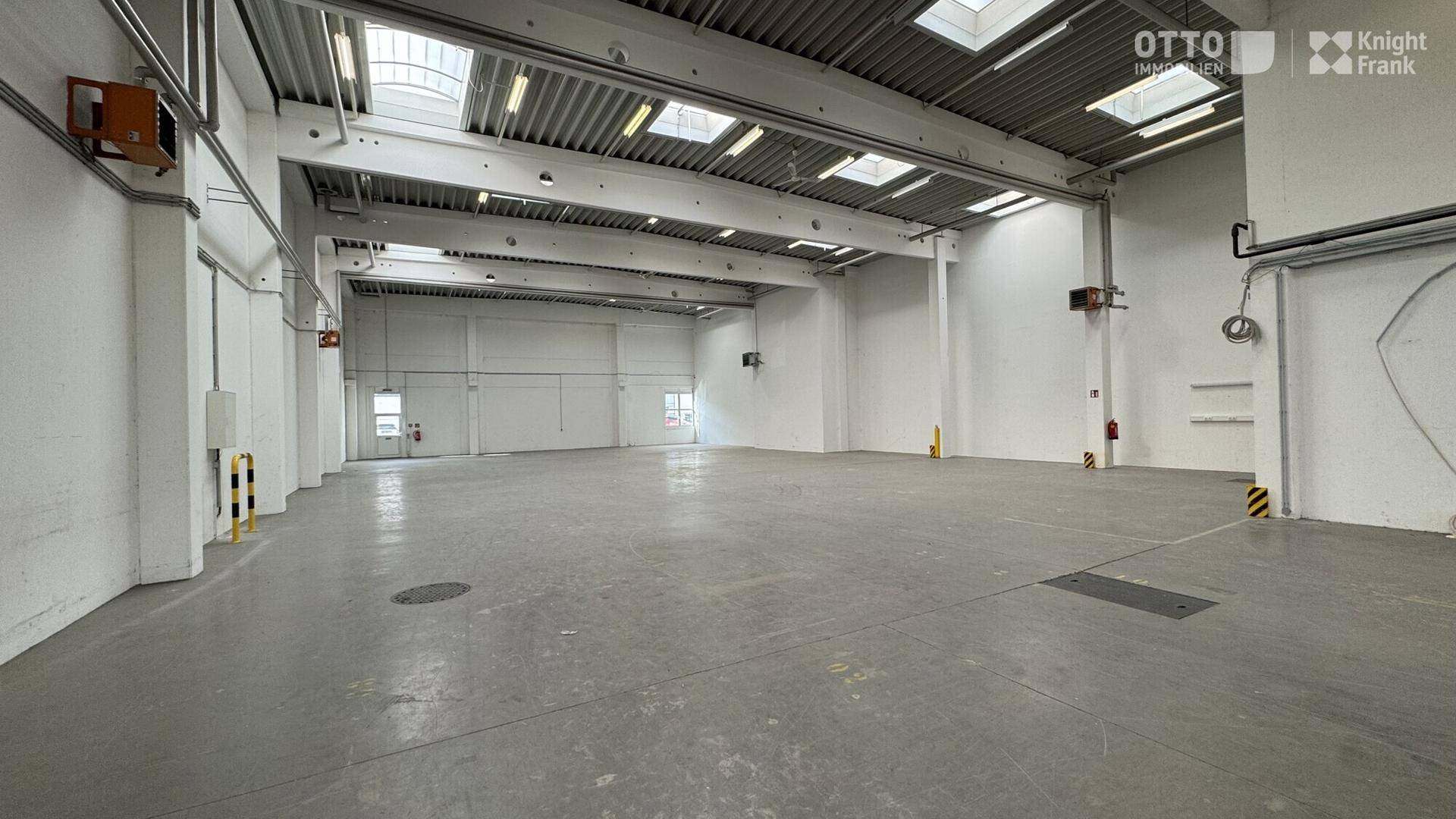 Große, leere Lagerhalle mit hohen Decken, Oberlichtern und Betonboden, bereit für neue Mieter.