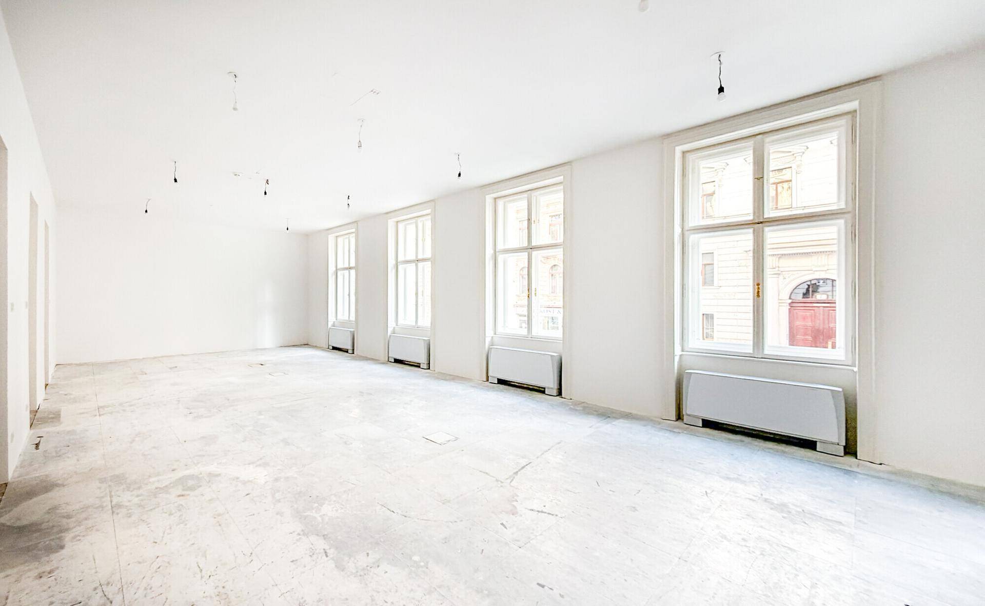 Großer, leerer Raum mit mehreren Fenstern und Heizkörpern, ideal für Büros oder Geschäfte in der Stadt.
