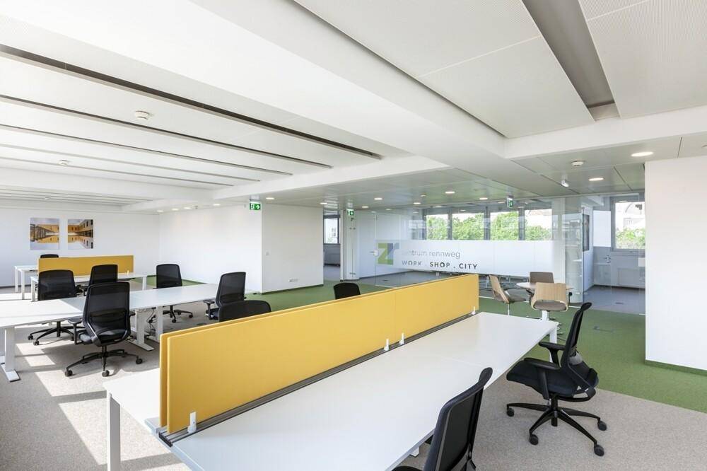 Geräumiges, modernes Großraumbüro mit gelben Trennwänden, weißen Schreibtischen und ergonomischen Bürostühlen.