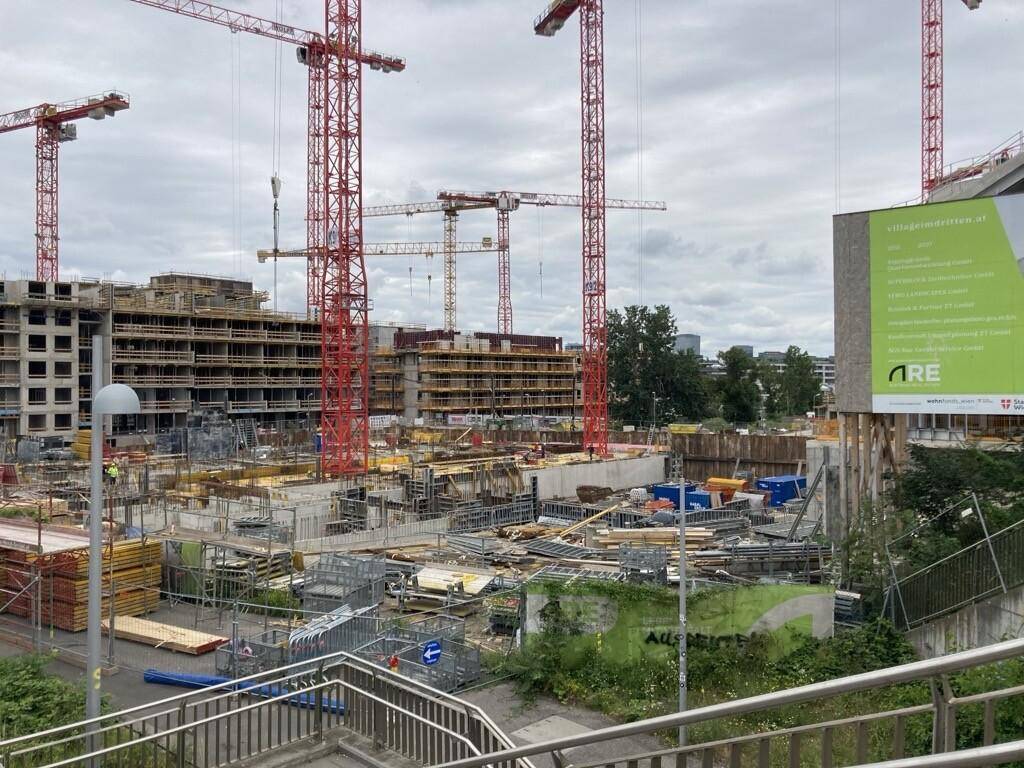 Baustelle mit mehreren Kränen und im Bau befindlichen Gebäuden unter bewölktem Himmel.