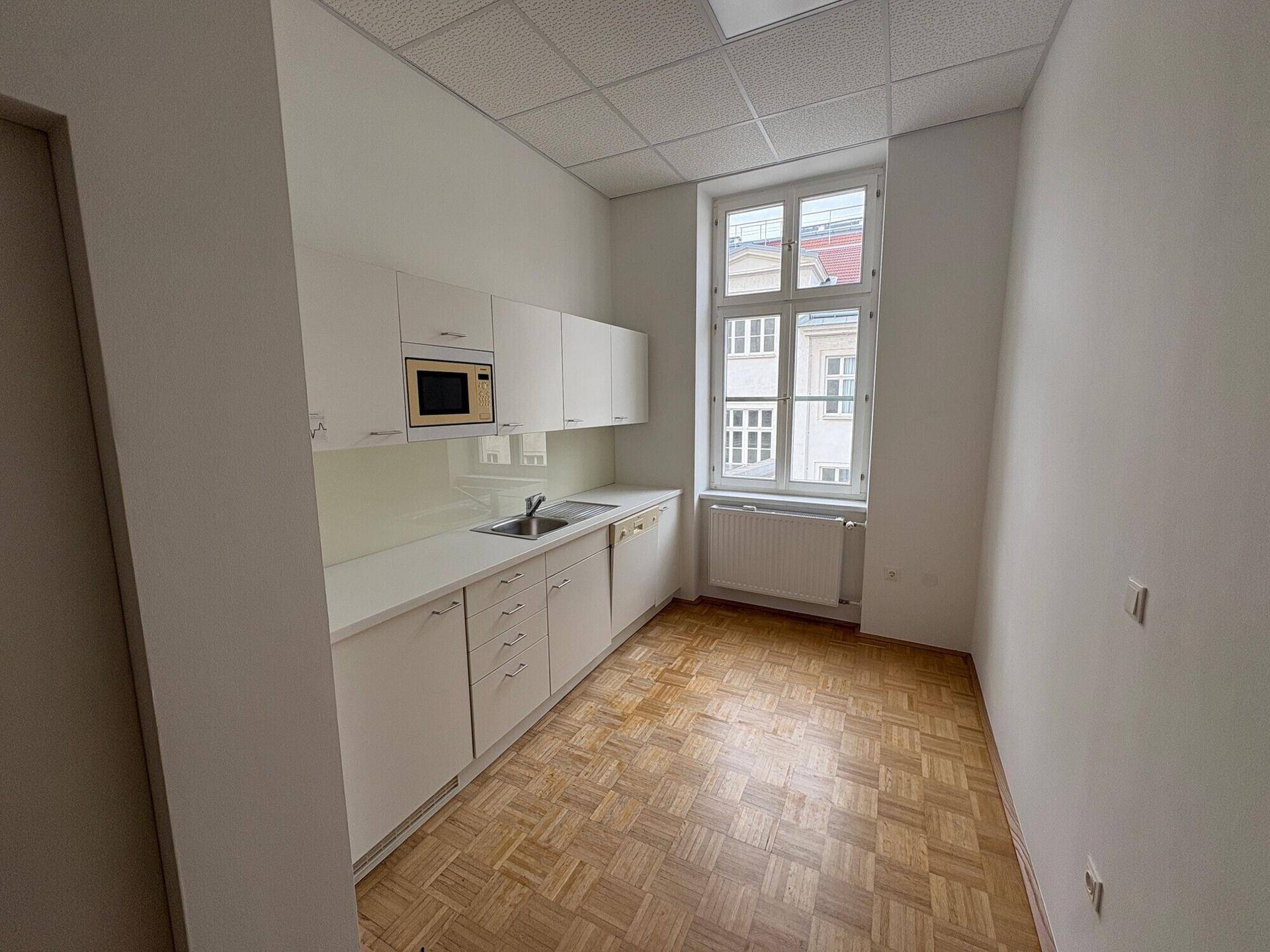 Kleine Küche oder Kochnische mit weißen Schränken, Spüle, Mikrowelle und Fenster, mit Parkettboden.