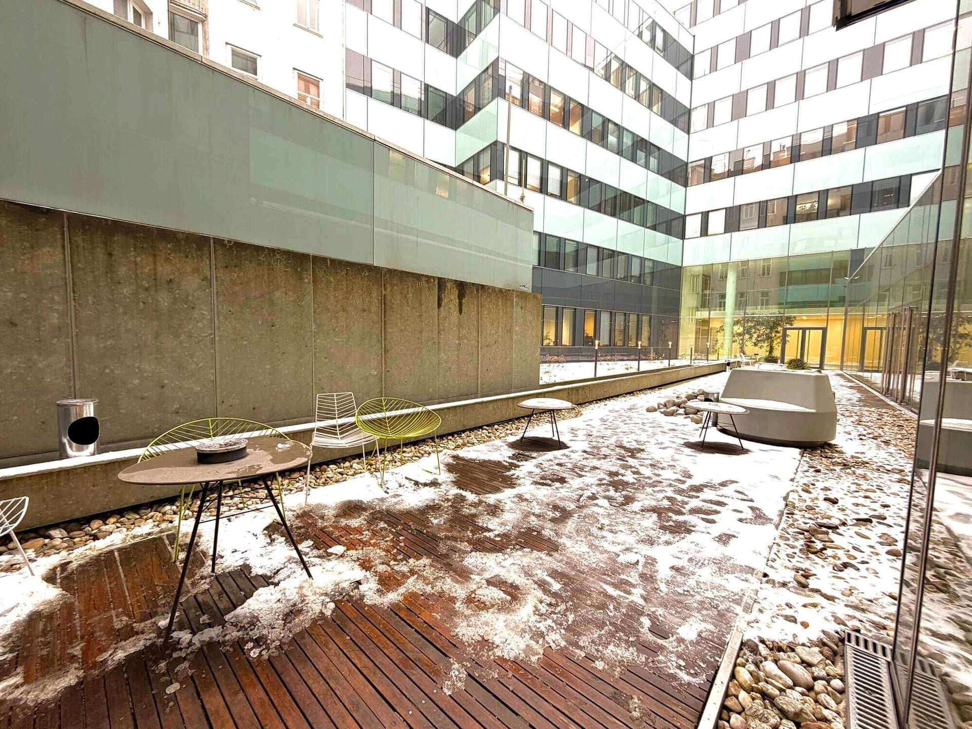 Moderne Außenterrasse mit Holzdeck und Sitzgelegenheiten, umgeben von Bürogebäuden.