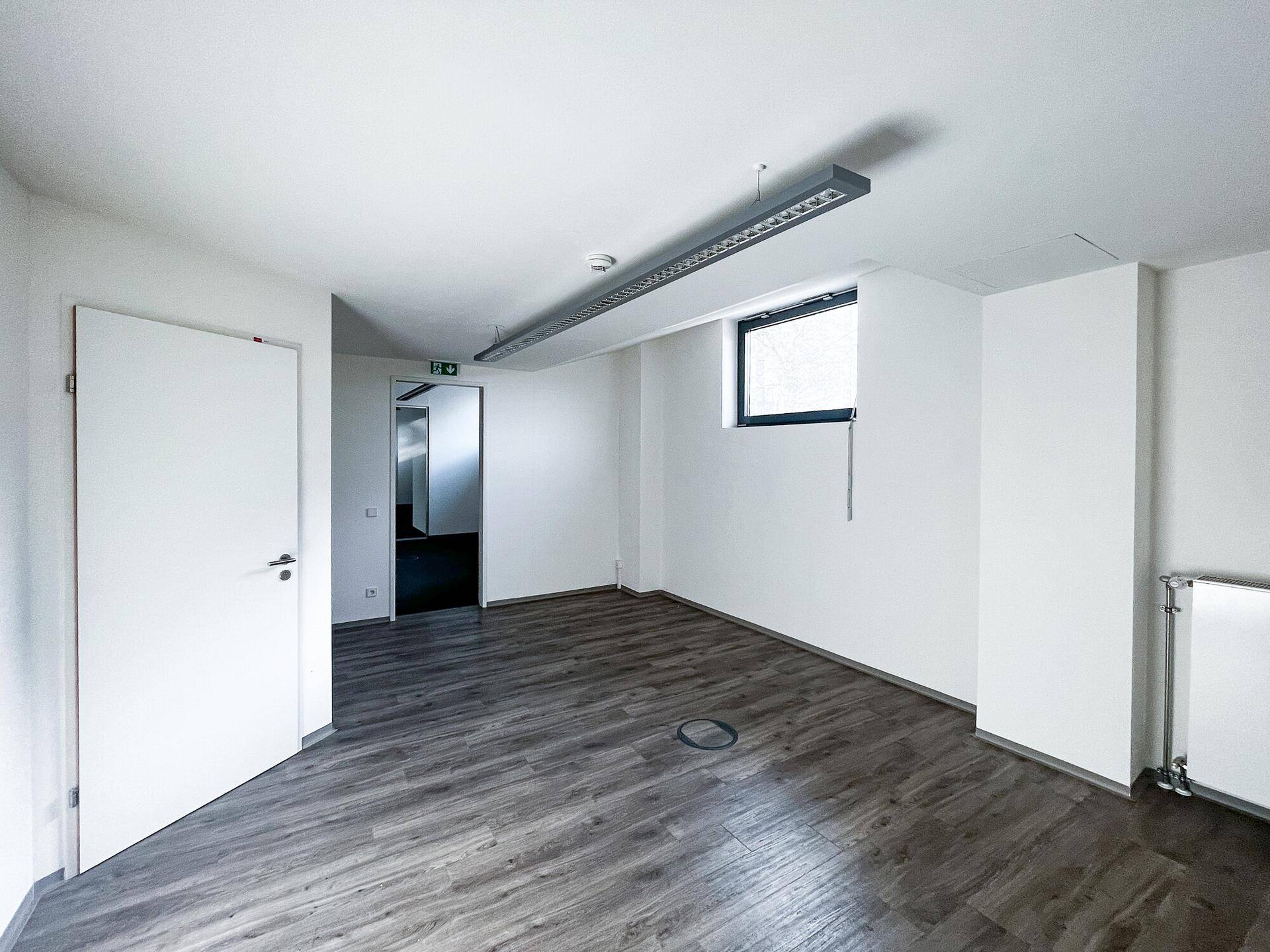 Renovierter Büroraum mit modernem Laminatboden und weiß gestrichenen Wänden, bereit zur Nutzung.