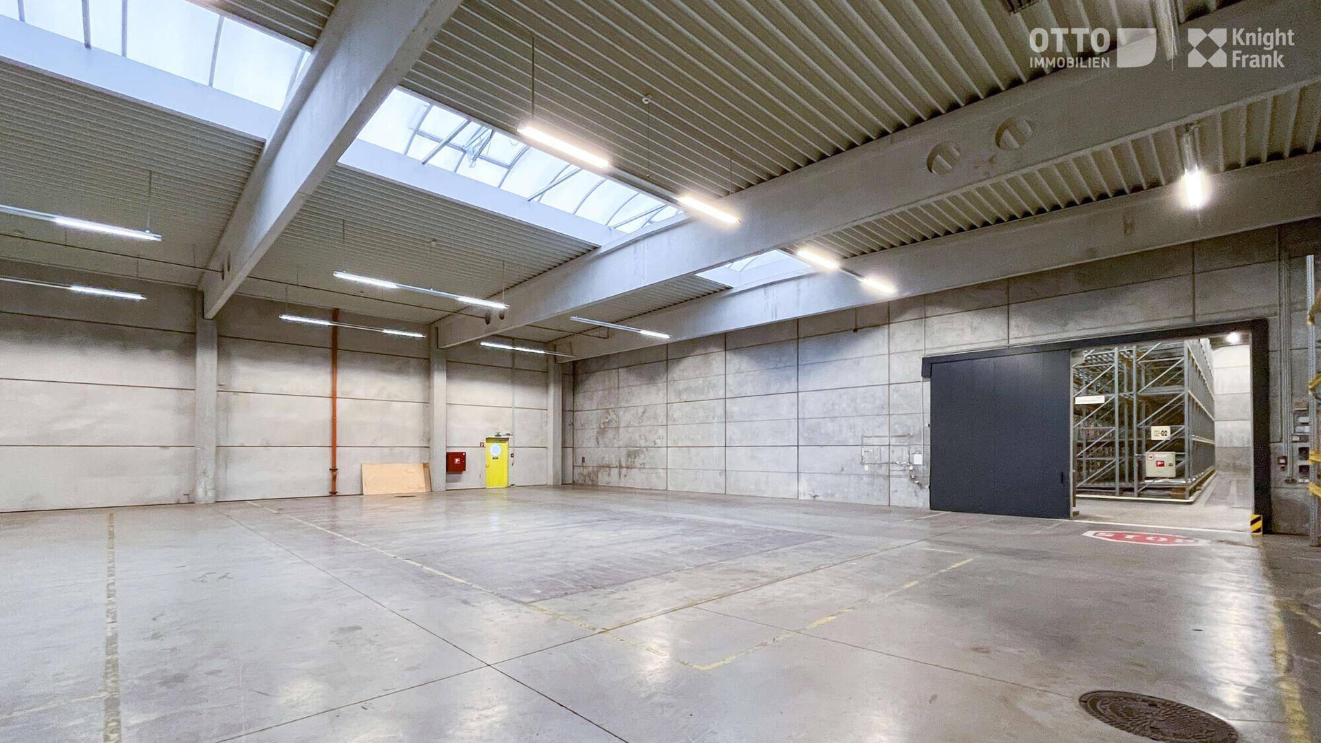 Geräumige Lagerhalle mit Betonboden, Oberlichtern und einem großen Schiebetor, bereit zur Nutzung.