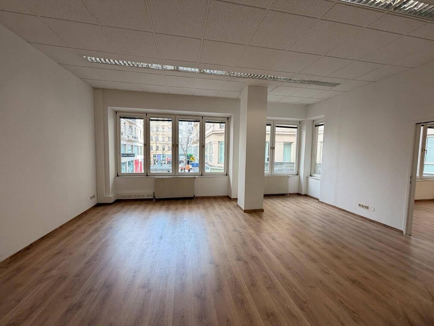 Helles Büro mit Laminatboden, großen Fenstern und Blick auf die umliegenden Gebäude und Straßen.