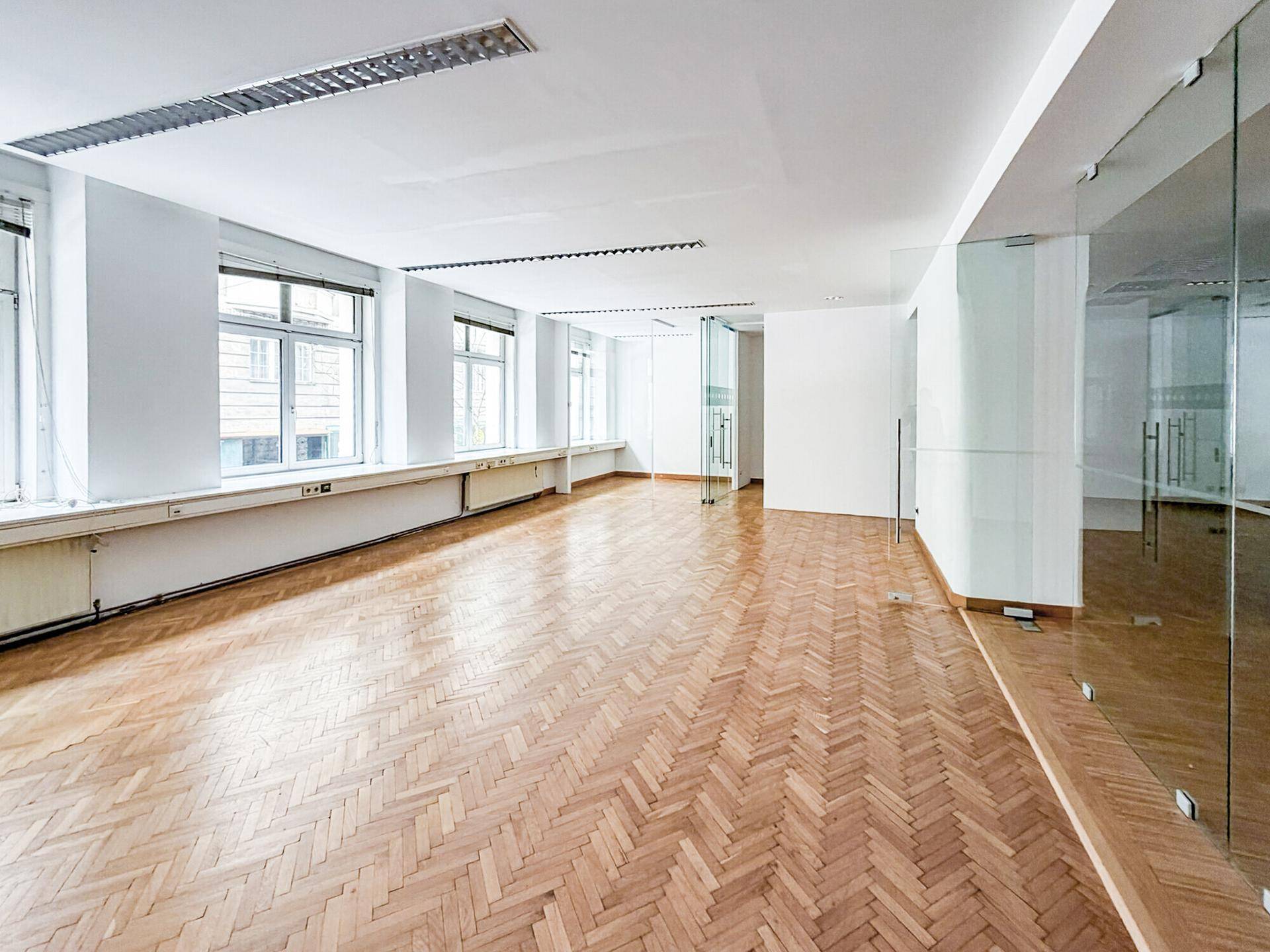 Weitläufiger Bürobereich mit Fischgrätparkett und Glastrennwänden, der vielseitige Gestaltungsmöglichkeiten bietet.
