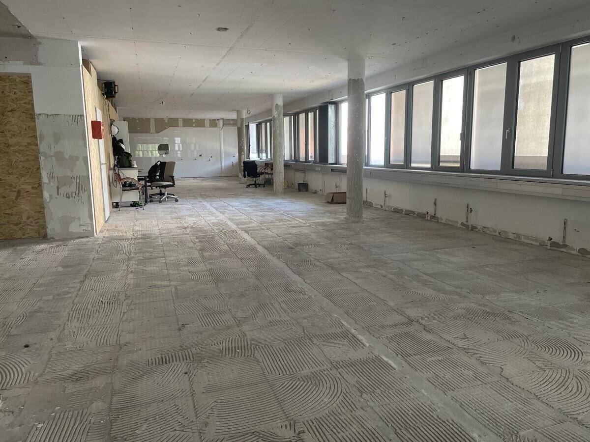 Großer, offener Gewerberaum in Renovierung mit Betonboden und großen Fenstern.