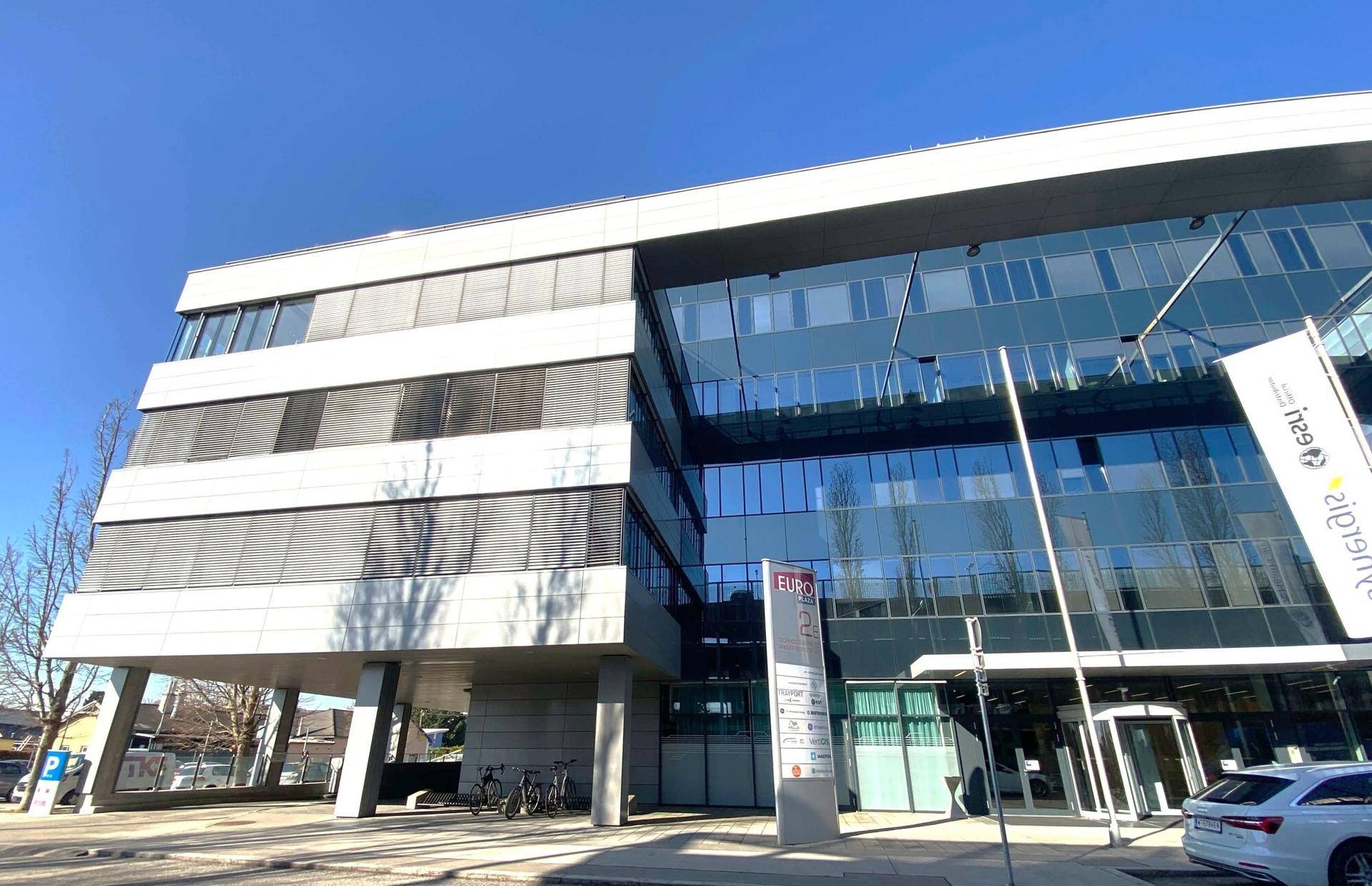 Modernes Bürogebäude mit Glasfassade und klaren Linien unter blauem Himmel.