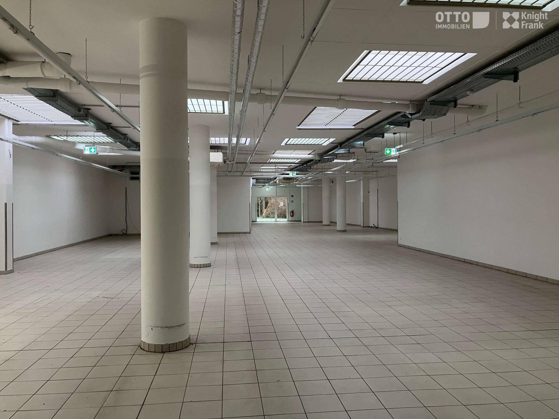 Großer, offener Gewerberaum mit Säulen, Fliesenboden und sichtbaren Deckeninstallationen, ideal für verschiedene Nutzungen.