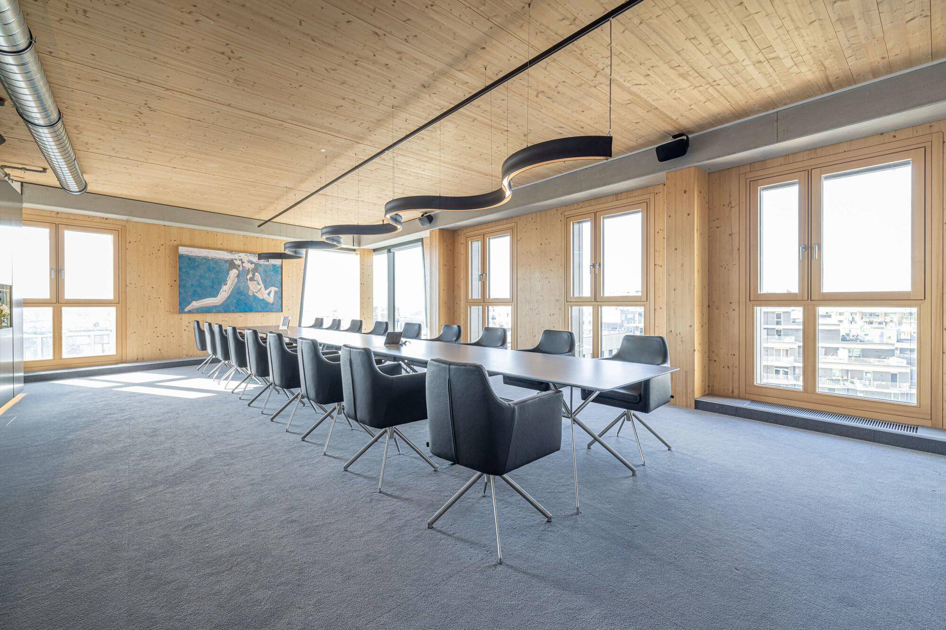 Geräumiger Konferenzraum mit Holzwänden und -decke, großen Fenstern und moderner Beleuchtung.