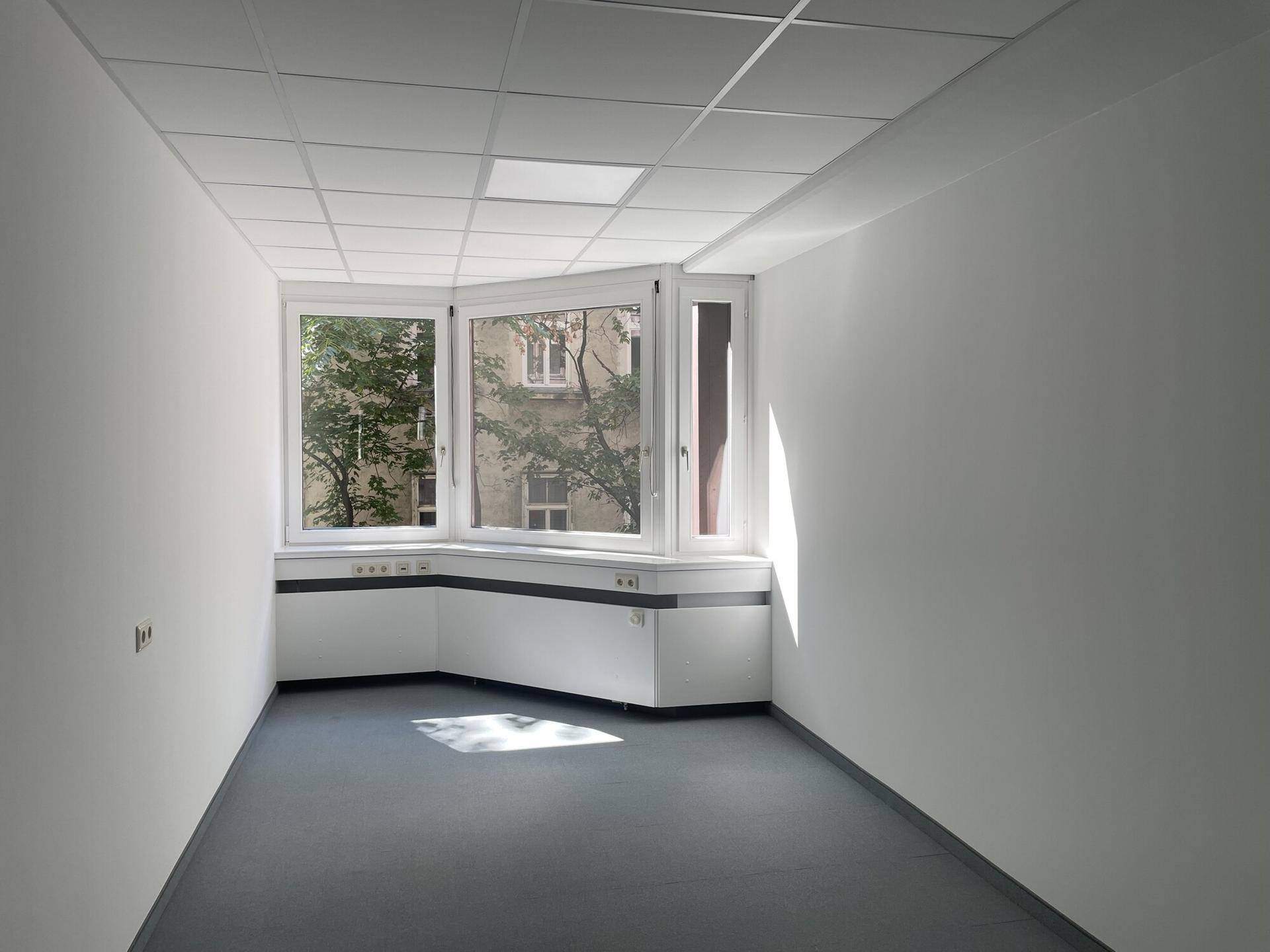 Heller Büroraum mit großen Fenstern, die viel Tageslicht hereinlassen und einen grünen Ausblick bieten.