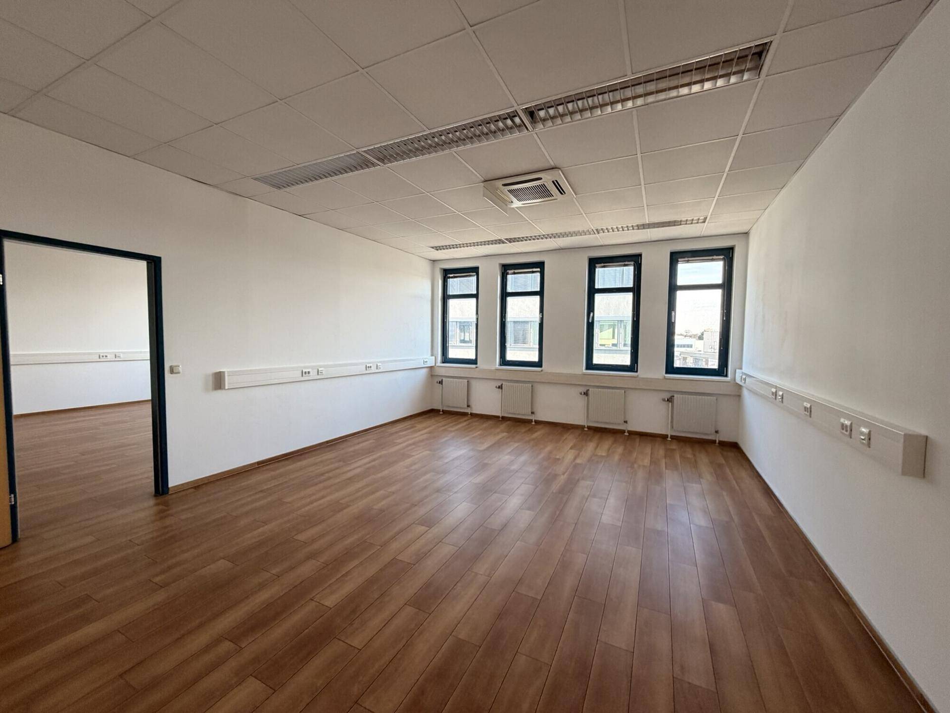 Leerer Büroraum mit Holzboden und mehreren Fenstern, ideal für flexible Arbeitsplatzgestaltung.