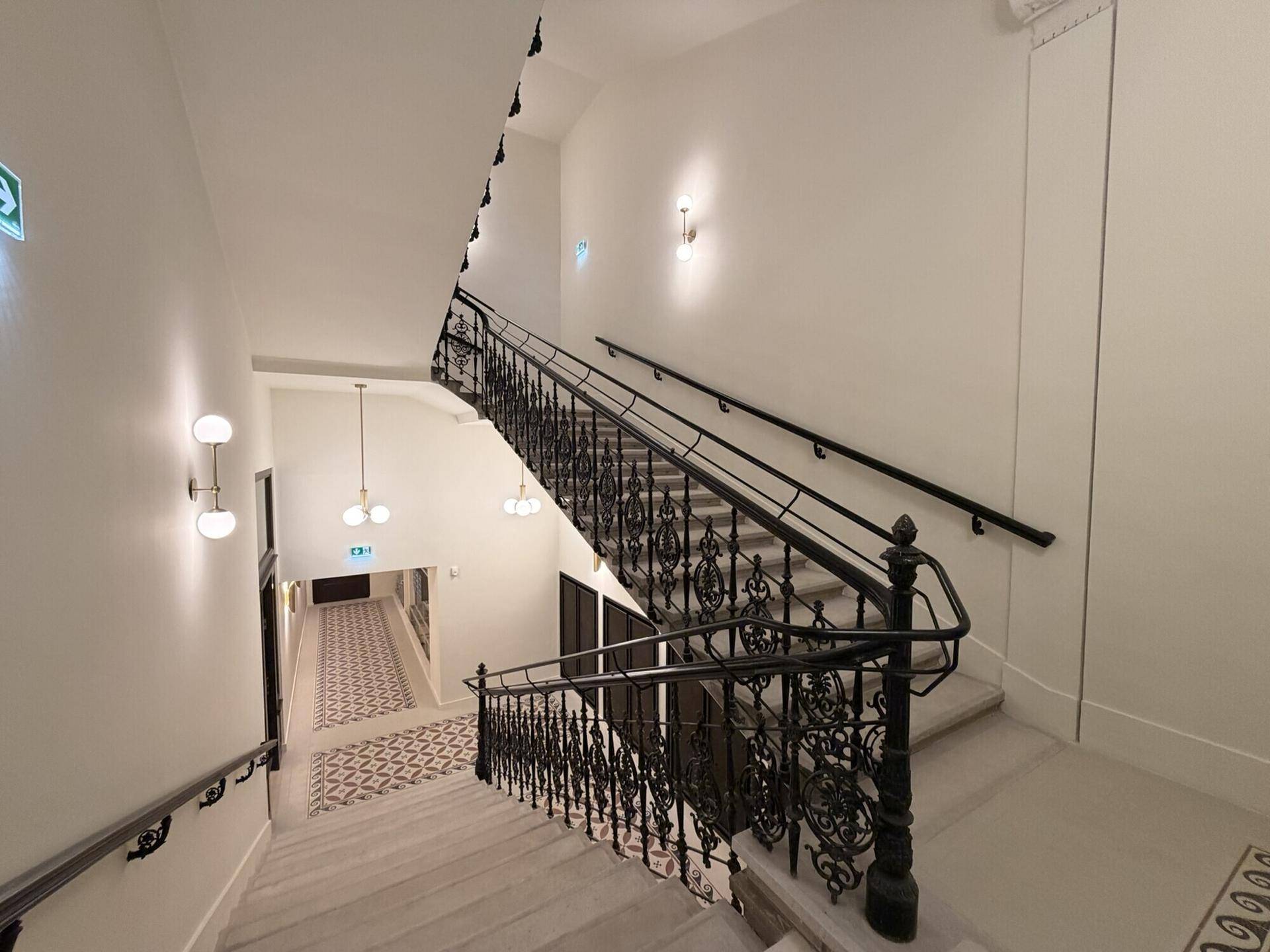 Elegantes Treppenhaus mit schmiedeeisernem Geländer und gemusterten Fliesen, das den Charme des Altbaus unterstreicht.